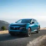 Front left 3/4 view of a blue 2025 Nissan Murano parked on a hill overlooking the ocean with other hills beside.